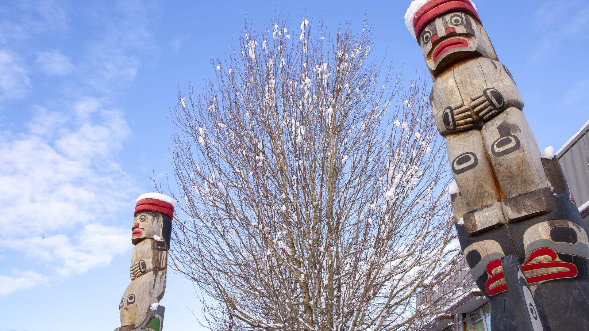 Two totem poles and a tree partially covered in snow.