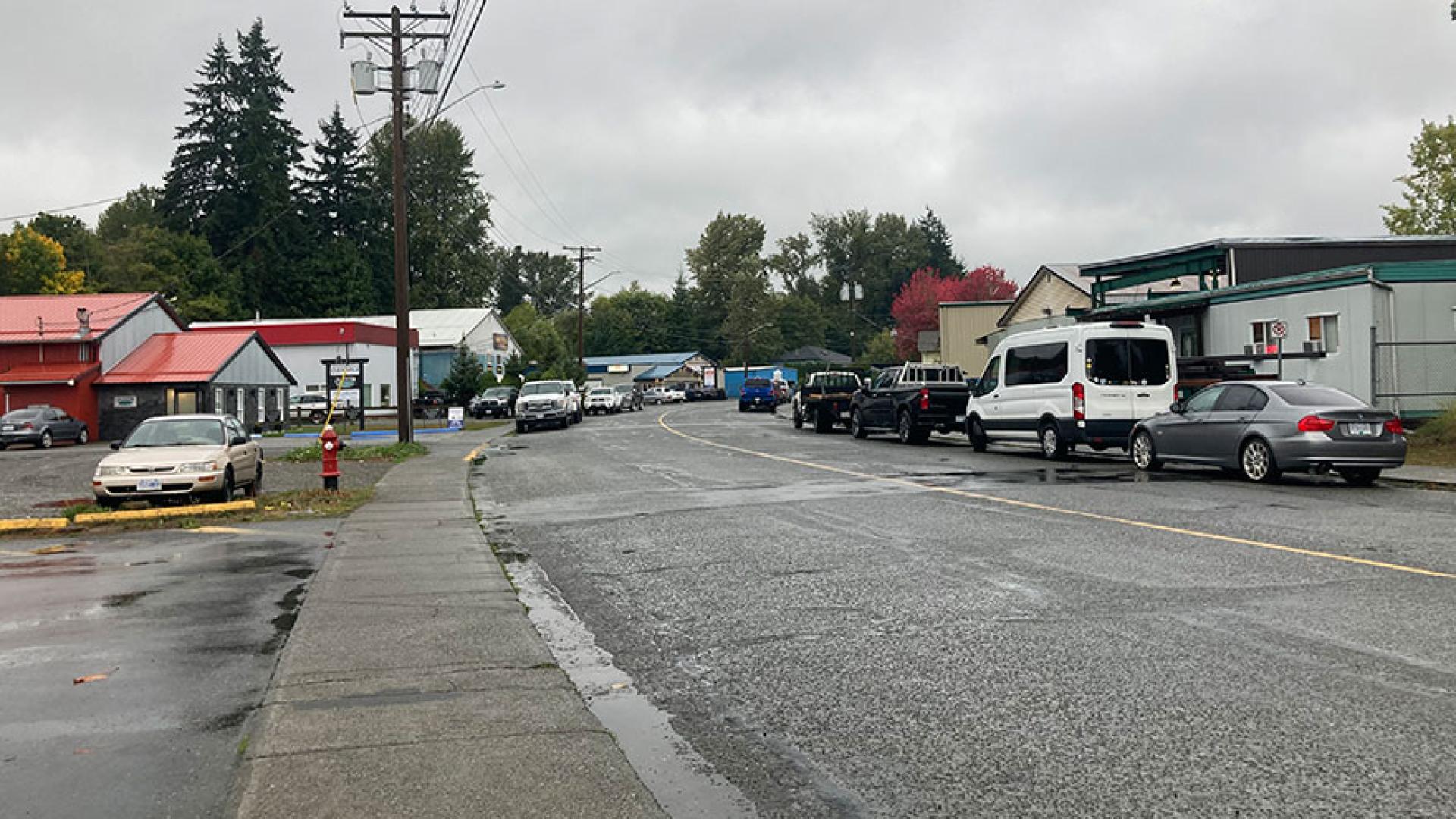 Cousins Avenue streetscape on a cloudy, wet day. There are cars parked on either side of the road and various businesses.