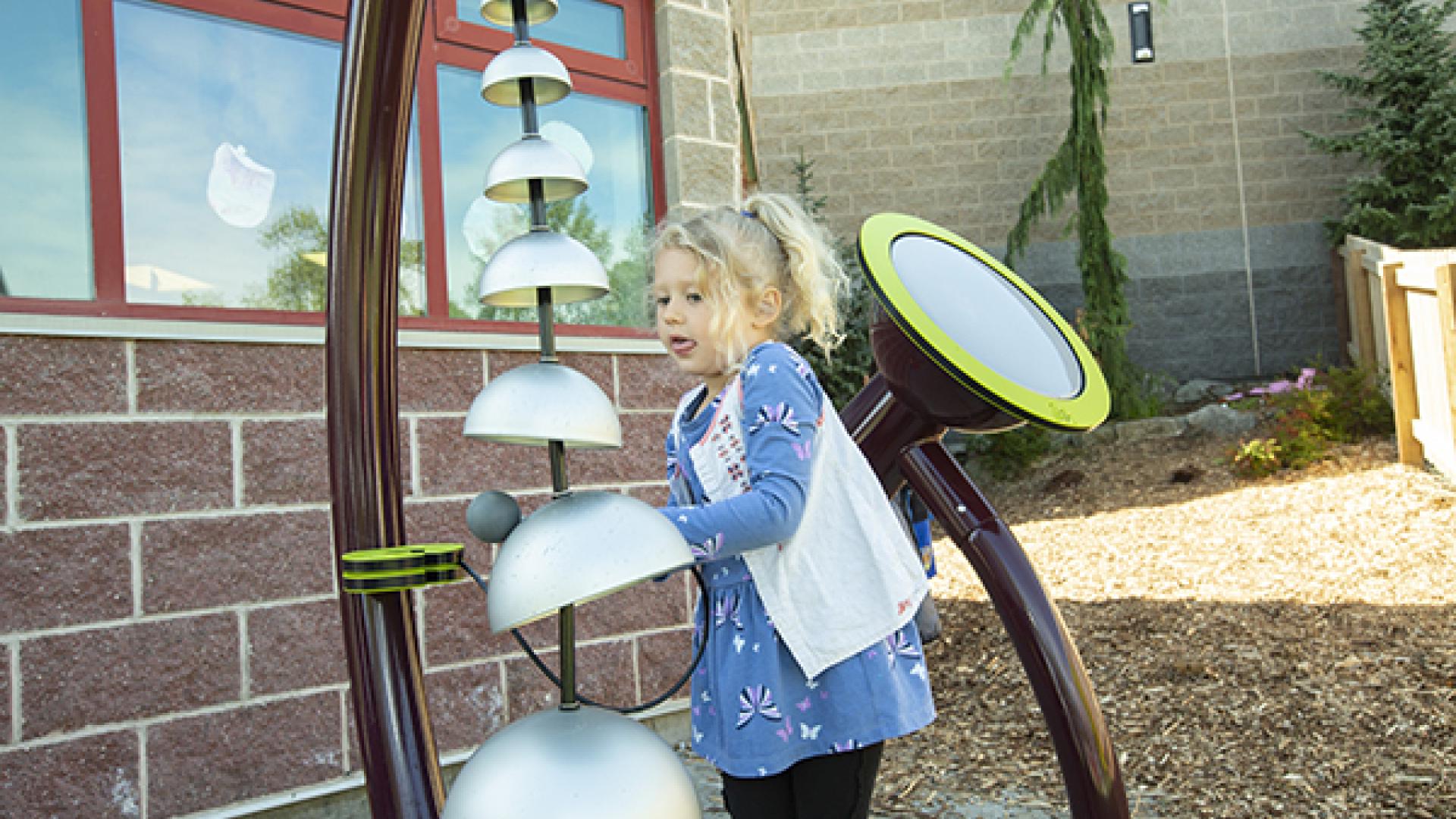 A girl playing outdoors with bells in the play space
