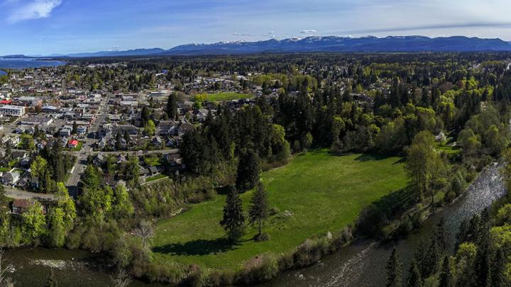 Aerial view of McPhee Meadows and the Puntledge River, looking south toward City of Courtenay, mountains and blue sky.