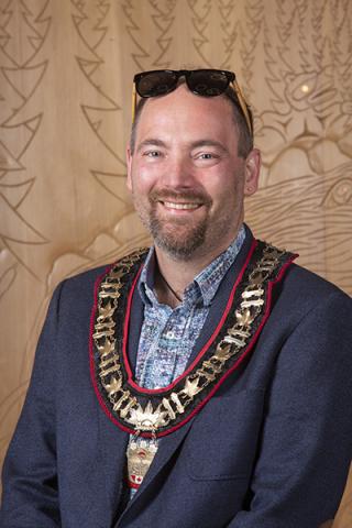Headshot of Mayor Bob Wells, a smiling man posing in front of a wood-carved wall.
