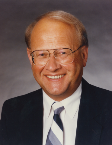 Headshot of Stan Hagen. There is a smiling man wearing glasses and a suit, shirt and tie.