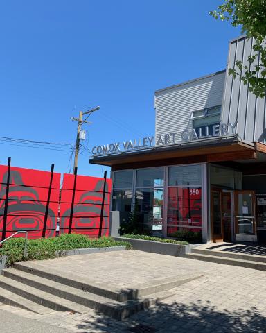 Exterior of Comox Valley Art Gallery. There is a glass door entrance and a red mural with first nations art on it.