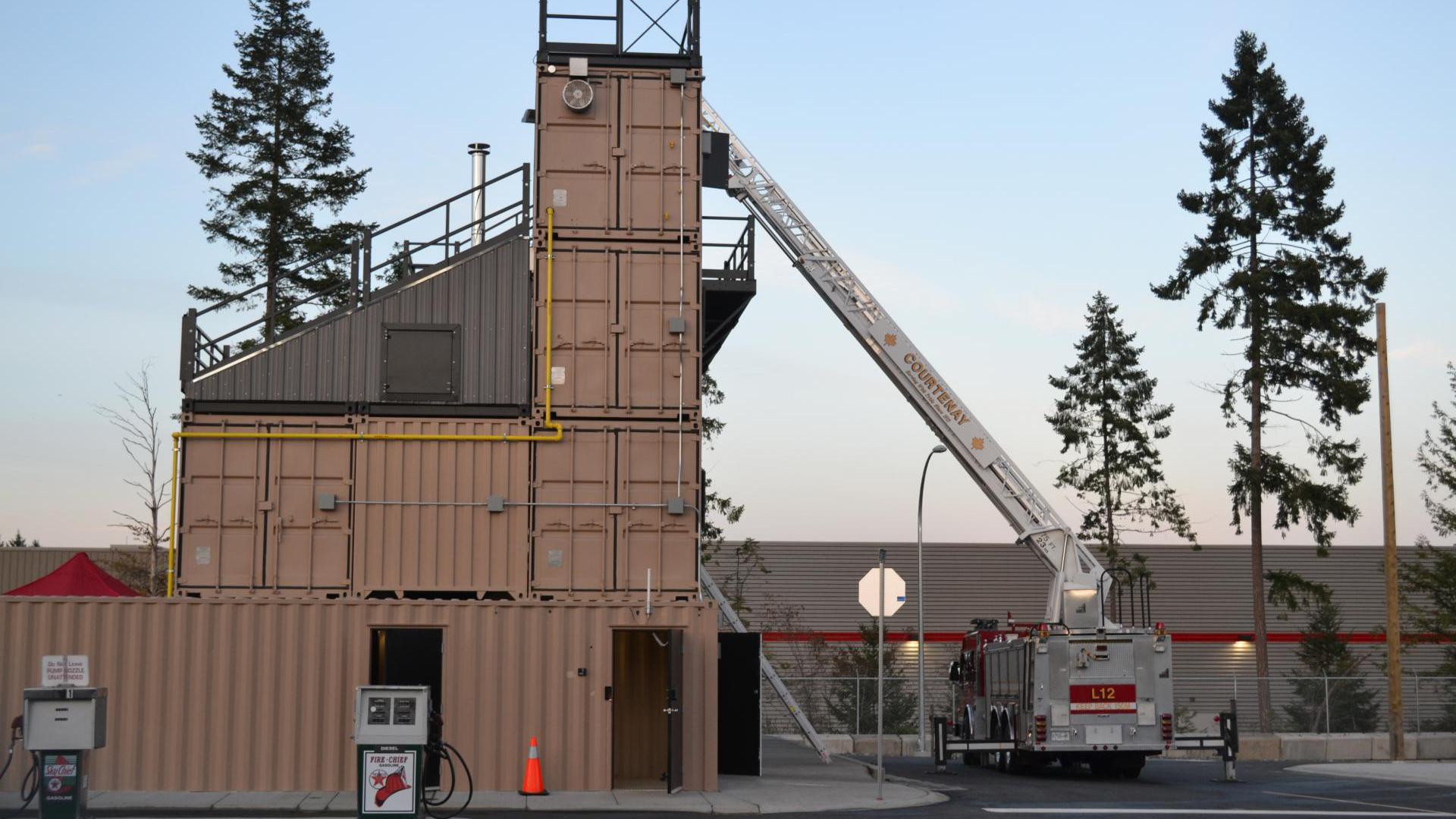 W.A. Lane Macdonald Fire Training Centre, a four-storey training facility made of shipping containers. A ladder truck is fully extended to the top floor.