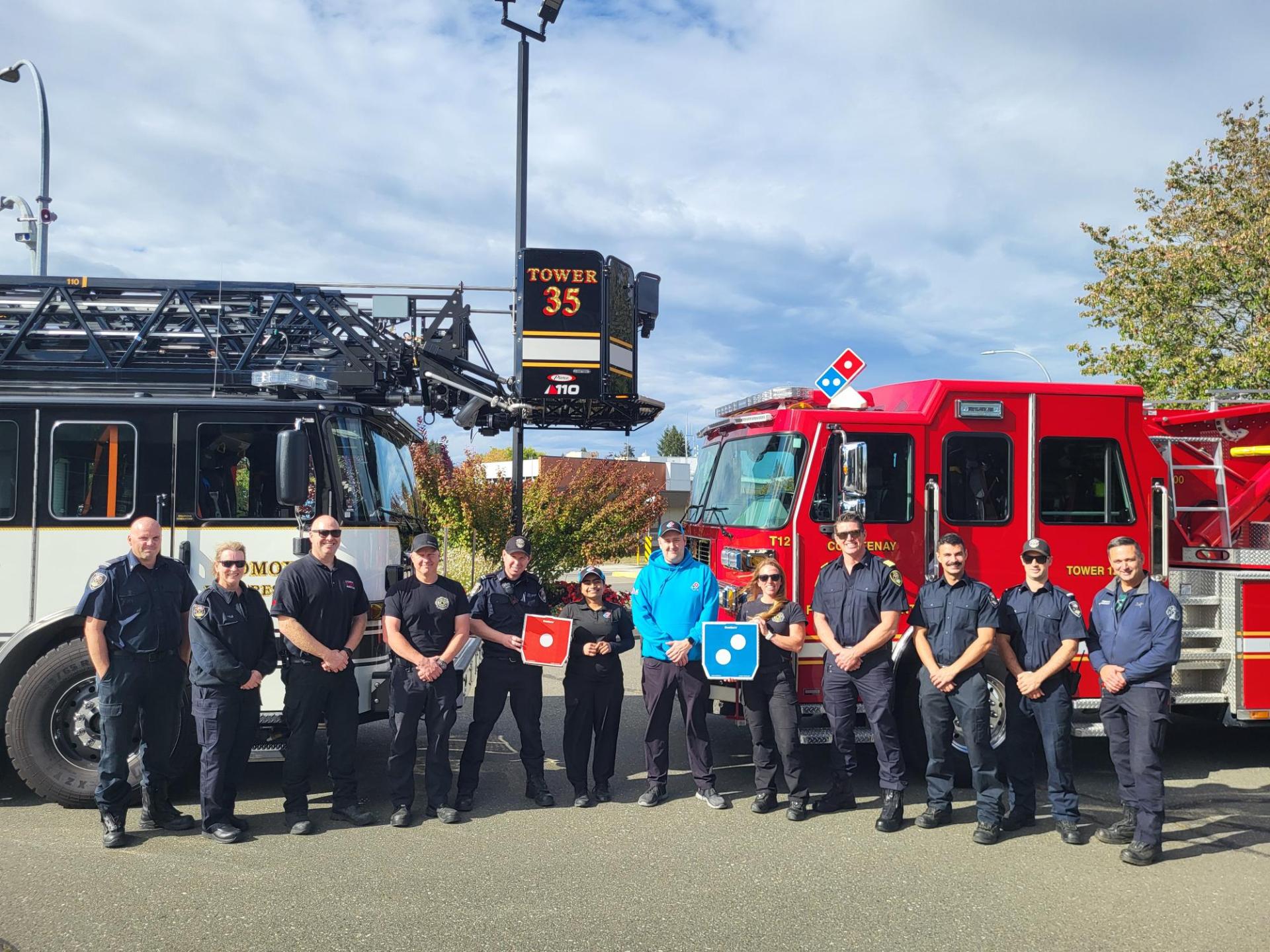 Courtenay and Comox fire departments stand in front of their fire trucks, flanking Dominos Pizza delivery drivers